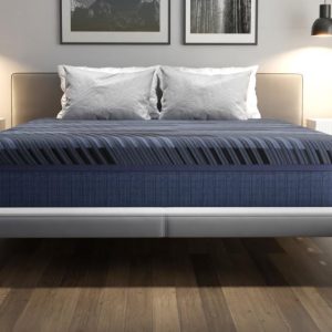 A modern bedroom showcases a large bed with blue-striped Southerland's Talliston Mattress and white pillows. Flanked by two white nightstands with lamps and minimal decor, a soft neutral headboard complements the wooden floor and minimalist artwork above.
