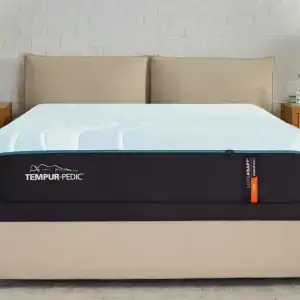 A Tempur-Pedic TEMPUR-LuxeAdapt® 13" Firm Mattress is displayed in a warmly decorated bedroom with beige walls, two wooden bedside tables, and matching lamps.