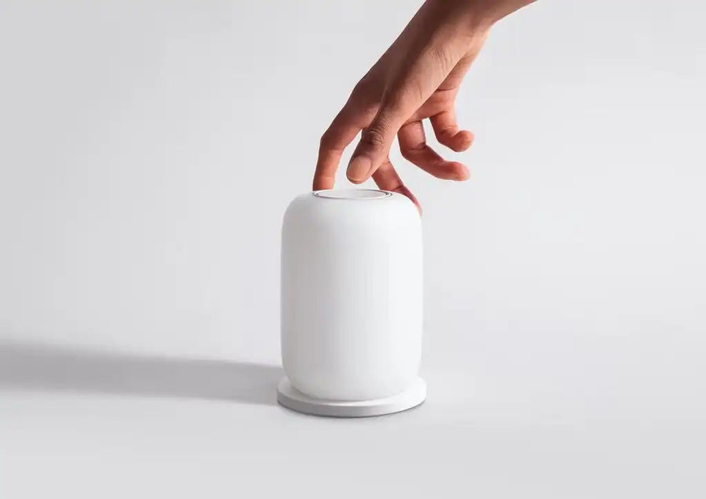 A person's hand pressing on the top of a minimalist white cylindrical device with Glow Light on a plain background.