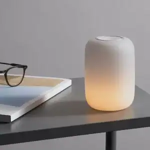 A modern, minimalist workspace featuring a Glow Light on a gray table beside a pair of glasses resting on an open book.