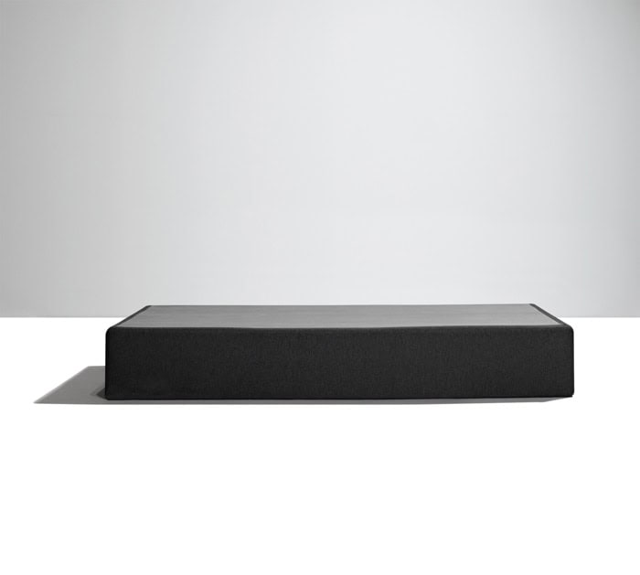 A minimalist, black rectangular platform with smooth surfaces, reminiscent of a Southerland 9" Semi Flex Box Spring, is seen against a plain, light background. The object casts a soft shadow on the white surface below it, emphasizing its geometric shape.