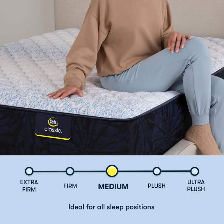 A person in light blue pants and a beige sweater sits on the edge of a Serta Classic Mattress. Below, a scale indicates the mattress is of medium firmness, described as "ideal for all sleep positions." The surface of the Serta Classic Mattress appears quilted and textured.