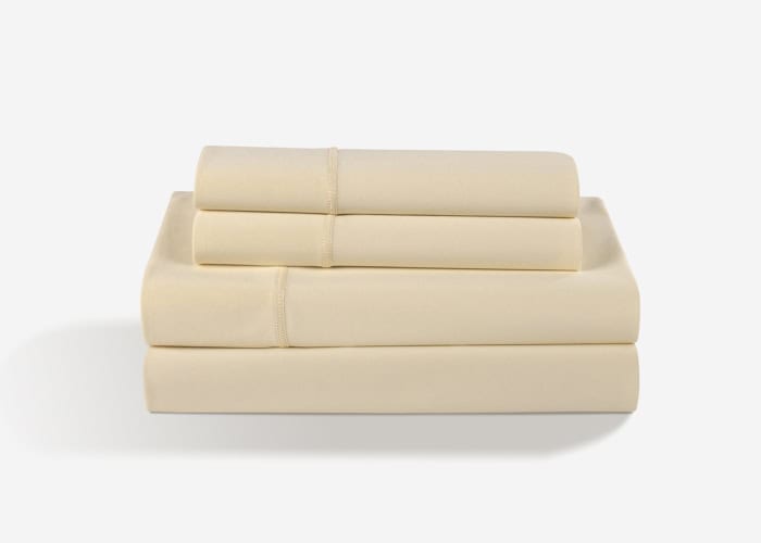 A neatly folded Dri-Tec Sheet Set, featuring a cream-colored design, is stacked in three layers. The set includes two smaller rectangular pieces positioned on top of two equally folded larger pieces, all displayed against a plain white background.