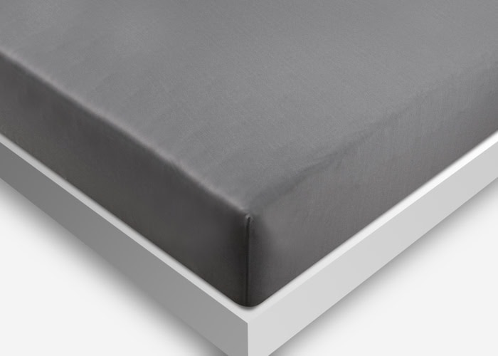 A close-up view of a neatly made bed featuring the Dri-Tec Sheet Set in gray on a white bed frame. The sheet set is smooth and tightly tucked around the mattress. The photo is taken from an angled perspective, highlighting the corner of the bed.