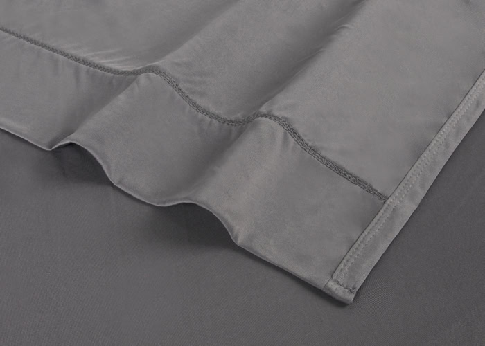 A close-up image of a folded grey Dri-Tec Sheet Set. The Dri-Tec material appears smooth and soft, with visible stitches along the edges and folds. The lighting highlights the texture, adding depth to the image, making it an exceptional addition to any bedding collection.
