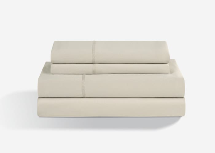 A neatly folded Dri-Tec Sheet Set in beige is displayed against a plain white background. The arrangement includes two pillowcases on top, a flat sheet in the center, and a fitted sheet at the bottom. The fabric looks soft and smooth.