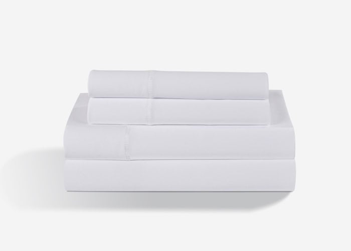 A neatly folded Dri-Tec Sheet Set, in pristine white, consisting of a flat sheet, fitted sheet, and two pillowcases, is stacked on a white background. The sheets are clean and crisp, emphasizing their smooth texture and precise folding.