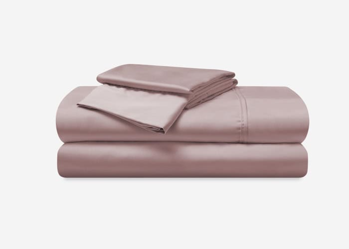 A neatly folded Hyper-Cotton Sheet Set in pink, which includes two pillowcases, a flat sheet, and a fitted sheet, displayed on a white background. The sleek and smooth appearance of the Hyper-Cotton material suggests a silky texture.