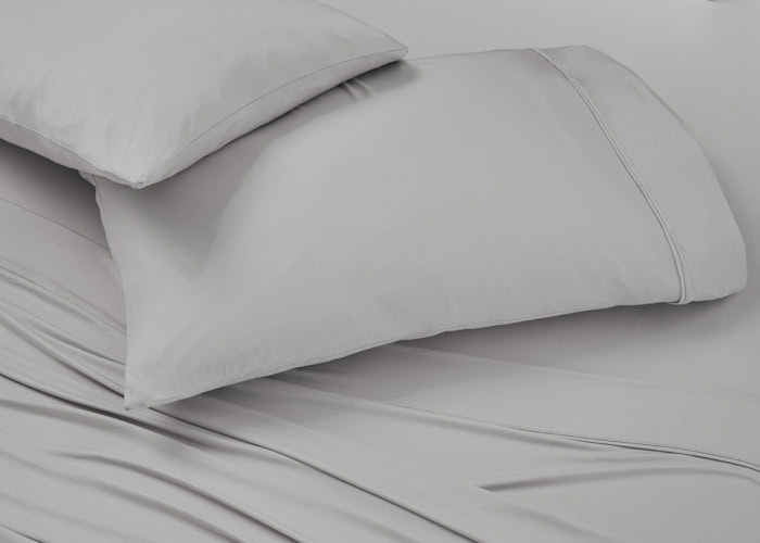 A neatly made bed with smooth, light gray cotton sheets and pillowcases from the Hyper-Cotton Sheet Set (Copy). The Hyper-Cotton fabric looks soft and slightly glossy, while the plump pillows rest invitingly at the head of the bed, creating a clean, minimalistic ambiance.