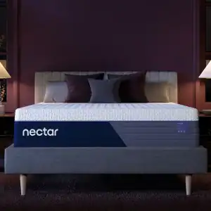 A modern bedroom showcasing a gray upholstered bed with a luxurious Nectar Luxe Memory Foam Mattress, adorned with dark purple and gray pillows. Two bedside tables and lamps sit on either side, all against a deep purple wall featuring two windows.