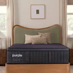 A modern bedroom with a wooden bed, green upholstered headboard, Purple RejuvenatePremier Mattress, and three decorative pillows. Light curtains frame the windows, and minimalist art hangs above the bed.