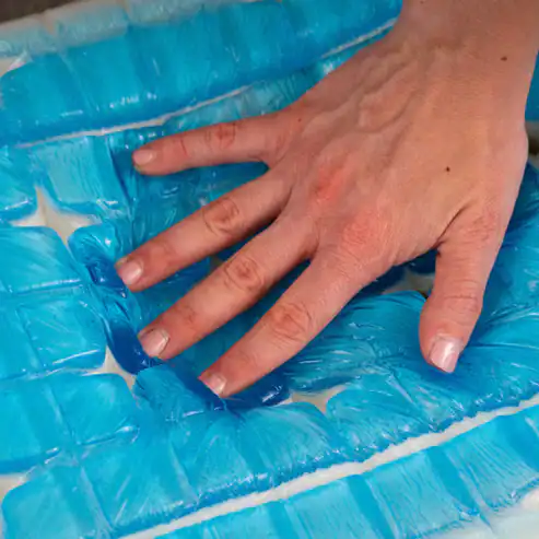 A hand presses onto the blue gel-filled surface of the Zecliner Model 2 Petite — Power Sleep Chair, making the gel shift and form indentations. The soft, flexible surface provides excellent comfort and support.