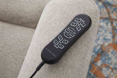 A black remote with white buttons rests on the arm of a light gray Zecliner Model 2 Petite — Power Sleep Chair, with part of a patterned rug visible in the background.
