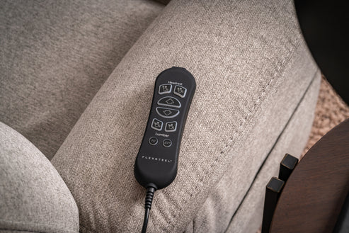 A black corded electronic remote with labeled buttons rests on the armrest of a light gray upholstered Zecliner Model 1 Power Sleep Chair, designed for adjusting seating positions.