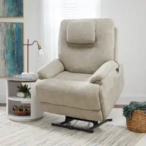 A Model 2 Plus Power Lift Recliner (Copy) in beige upholstery sits in a bright living room with light walls, art, a round side table, and woven rug. The chair is partially lifted for easy standing and comfortable support.