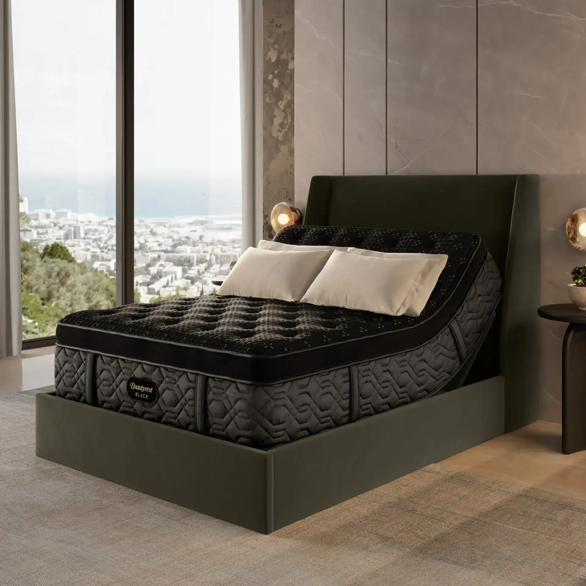 A modern bedroom features a large dark adjustable bed with a Beautyrest Black® Series One 13.5" Extra Firm Mattress, two white pillows, and floor-to-ceiling windows showcasing city and ocean views. The decor is contemporary with neutral tones.
