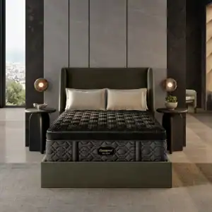 A modern bedroom with a dark upholstered bed frame features a Beautyrest Black® Series One 13.5" Extra Firm Mattress, two light pillows, black rounded nightstands, spherical lamps, and a large window revealing a city view.