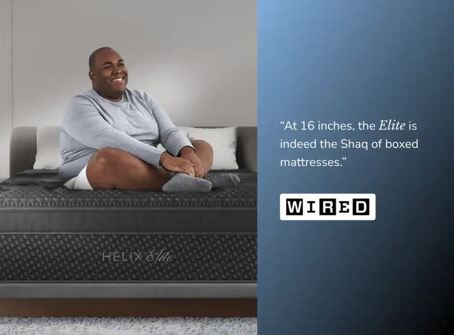 A smiling man in a gray shirt and white shorts sits cross-legged on a Helix Twilight Elite mattress. Beside him, a WIRED quote praises its size and comfort, calling it the "Shaq of boxed mattresses.