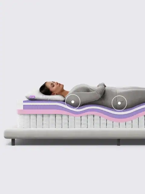 A woman in gray lies on her side atop the Purple Rejuvenate Mattress, shown in cross-section with purple, pink, and white foam layers that highlight pressure relief at her hip and shoulder.
