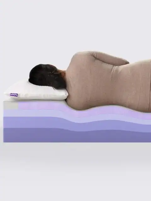 A person lies on their side with a white pillow atop the Zecliner Model 1 Power Sleep Chair, whose cross-section reveals wavy purple and blue layers that highlight its supportive and comfortable design.
