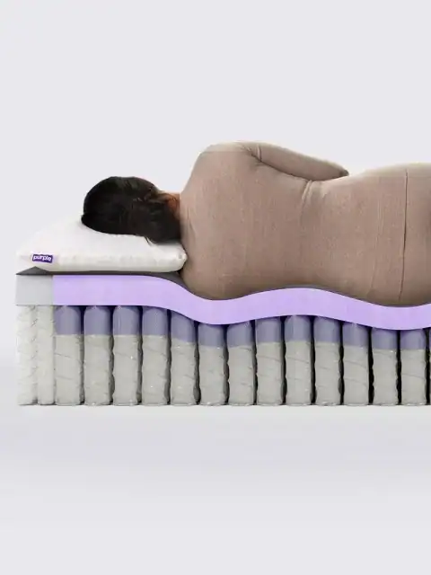 A person lies on their side on a Purple RestorePlus Hybrid Mattress, showing the visible purple and white layers as the hybrid mattress contours to the body’s shape for excellent support.