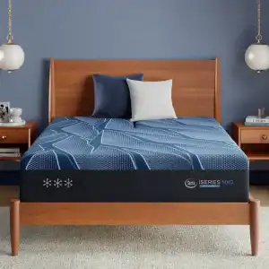 A modern bedroom with a wooden bed features a blue and white Serta iSeries NXG 3500 Hybrid — Firm mattress, two blue pillows, one white pillow, nightstands with books, and hanging globe lamps against a blue wall.