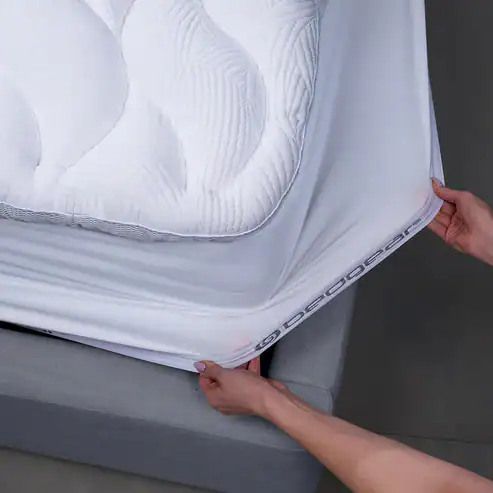 A person stretches a white React Pro Performance Mattress Topper over the mattress corner, fitting it smoothly and securely.