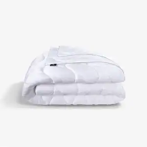 A neatly folded white Performance Comforter—medium weight with a subtle wave pattern—rests on a plain light background.