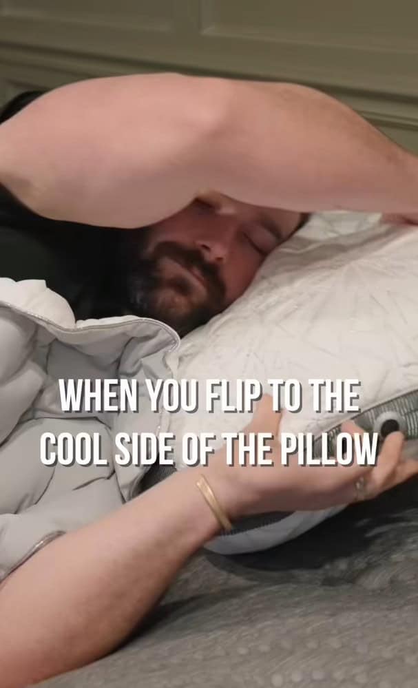 A man lies in bed, hugging a pillow with a content expression. Text on the image reads, "WHEN YOU FLIP TO THE COOL SIDE OF THE PILLOW.