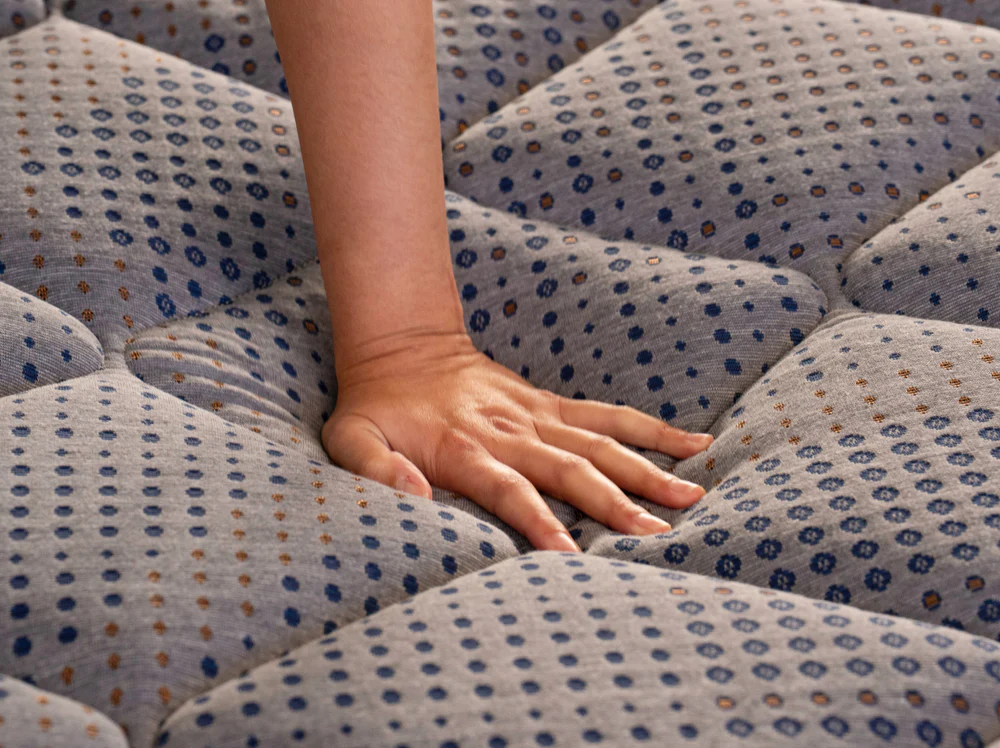 A hand presses on the CopperFlex Hybrid 12" mattress, showing its tufted top softly compressing under pressure to highlight the mattress’s cushioning and plush comfort.